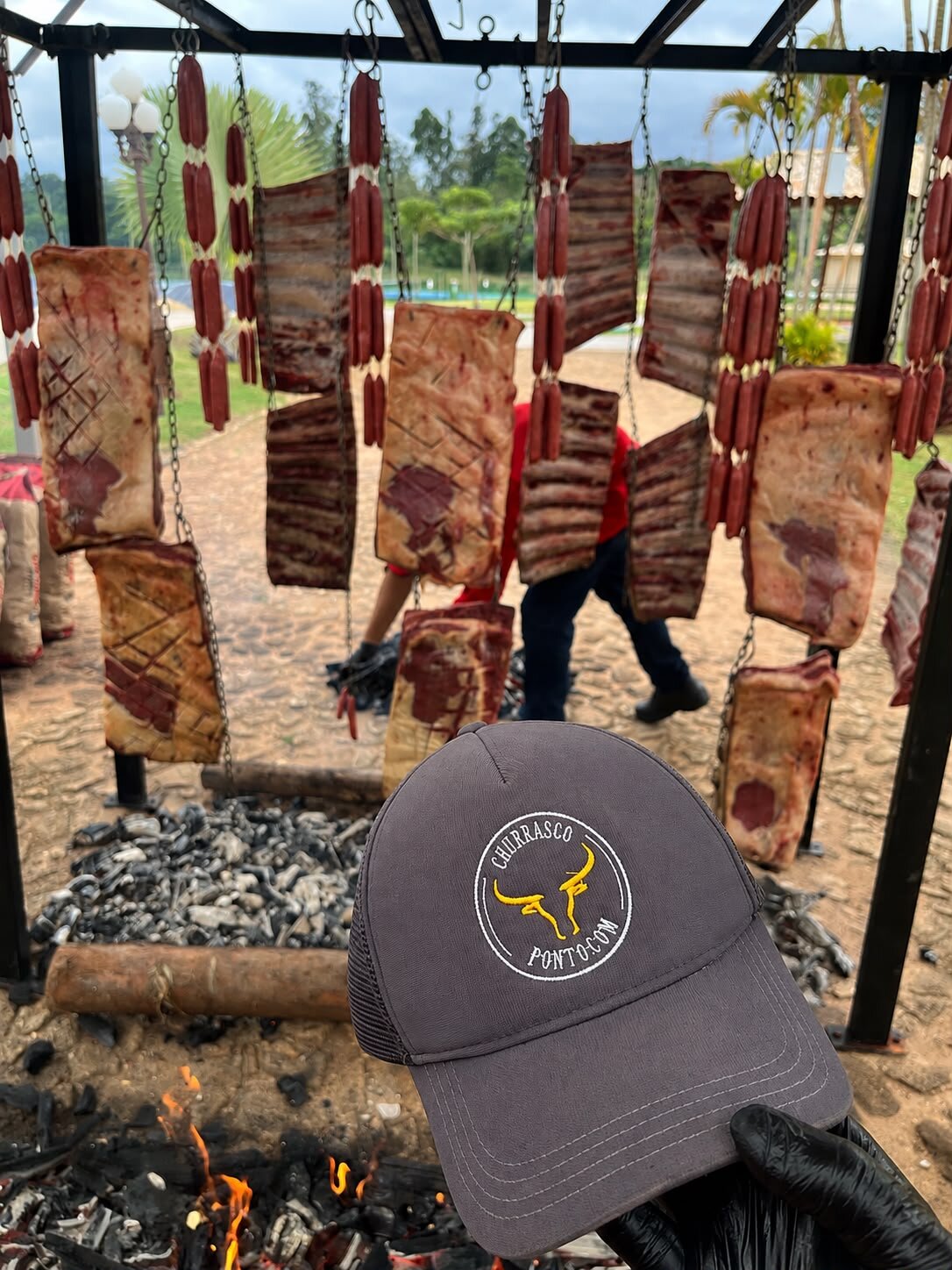 Fogo de chão montado a céu aberto em fazenda, com o boné da casa em primeiro plano
