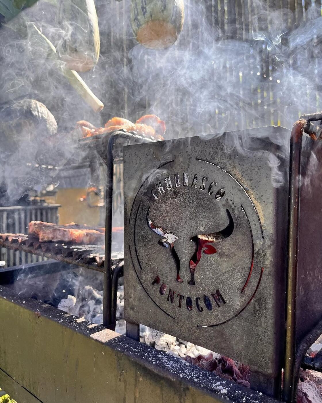 Chapa de ferro com o brasão do Churrasco Ponto Com sobre a brasa