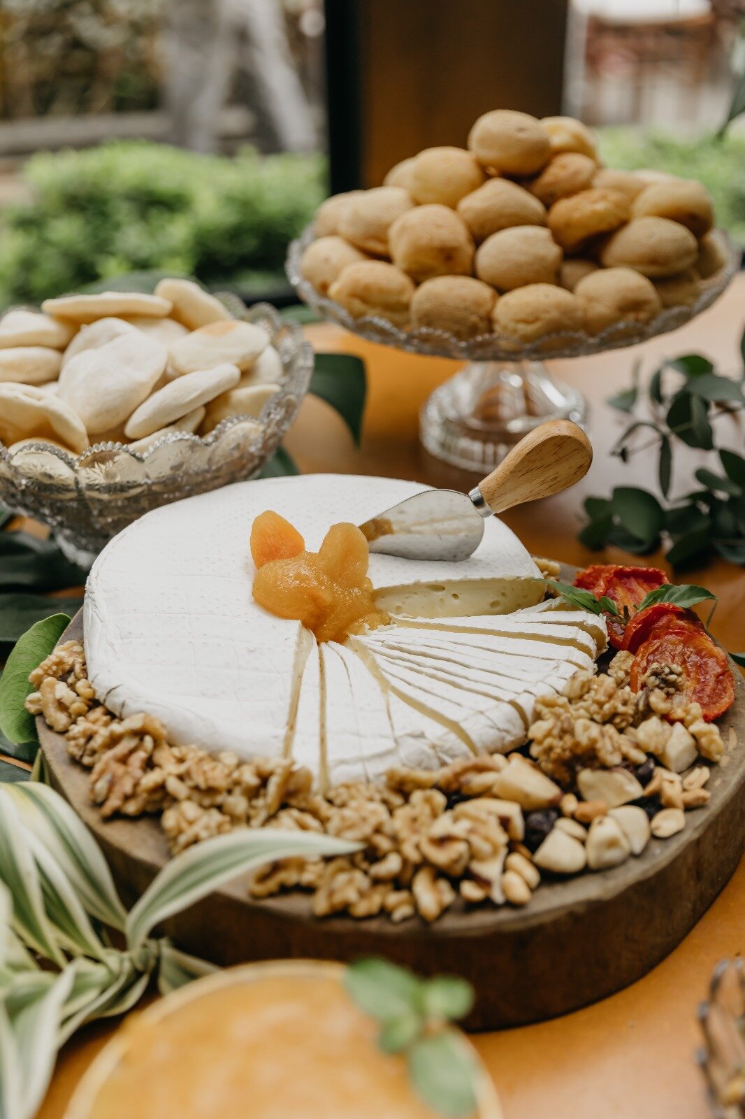 Mesa de frios com brie, damasco, nozes e pão de queijo em suportes de vidro